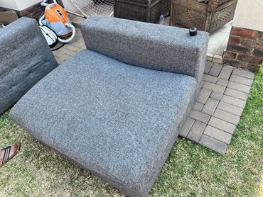 A gray fabric sofa seat cushion with a detached backrest outdoors.