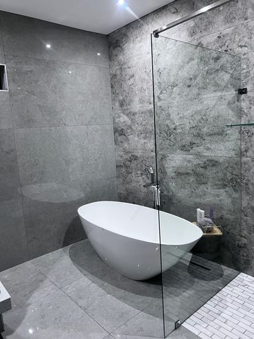 Modern bathroom with a freestanding white bathtub and gray stone walls.