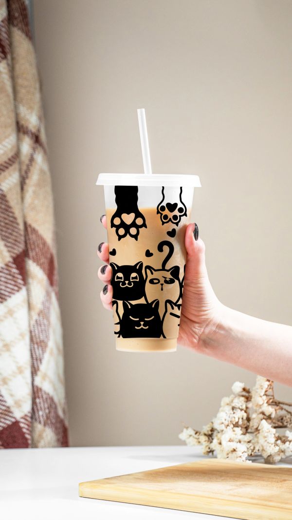 Hand holding a cup with cute cat designs.