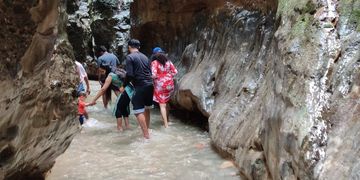 Group of people wading through a rocky water stream in a narrow canyon.