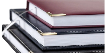 Stacked hardcover notebooks with gold corner protectors and ribbons.