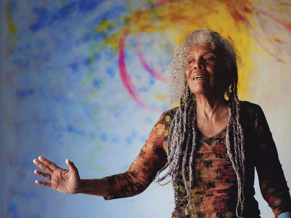 Elderly woman with gray dreadlocks gestures passionately.