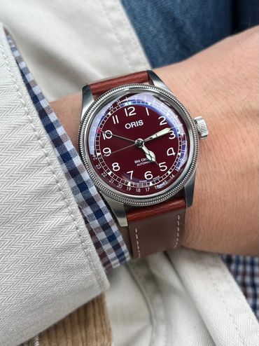 Oris wristwatch with burgundy dial and brown leather strap on a wrist.