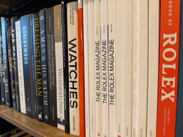 A bookshelf filled with books and magazines about watches and Rolex.