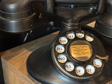 Close-up of a vintage black rotary dial telephone on a wooden surface.
