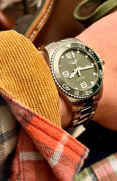 Close-up of a Longines wristwatch on a wrist with a plaid sleeve.