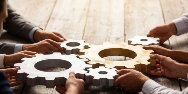 Hands holding interconnected gears on a wooden table.