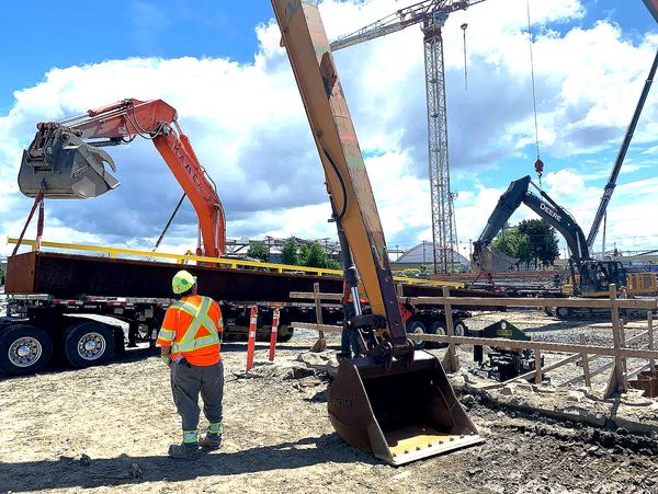 Construction worker overseeing heavy machinery lifting a large steel beam on site.
