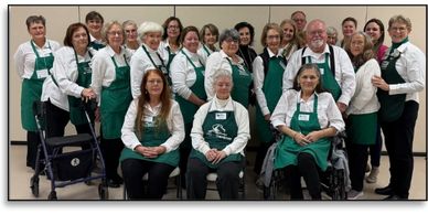 large group of people posing while wearing green aprons and white shirts