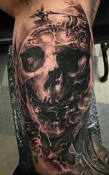 Realistic black and grey skull tattoo with mechanical elements on arm.