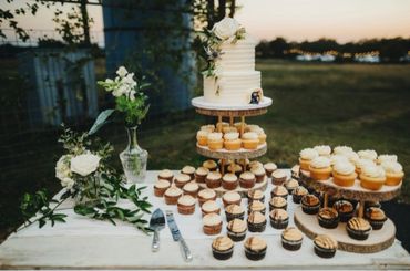 Wedding cake table with 2 tiered cake, variety of cupcakes, and flowers.