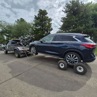 Daytime roadside breakdown assistance towing an SUV with a wheel-lift dolly in a neighborhood
