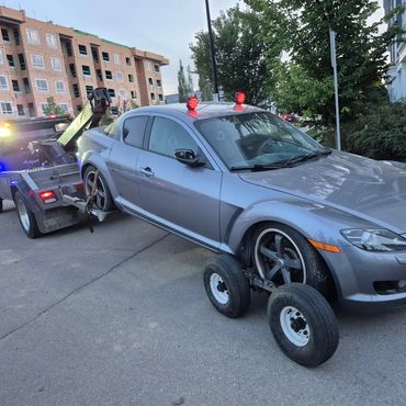 24/7 roadside assistance, towing a red SUV with a wheel-lift dolly in a commercial parking lot.