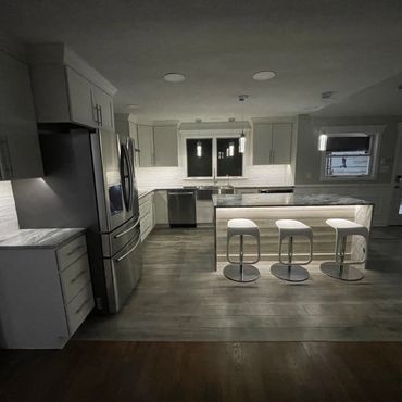 Modern kitchen with island and three white bar stools under soft lighting.