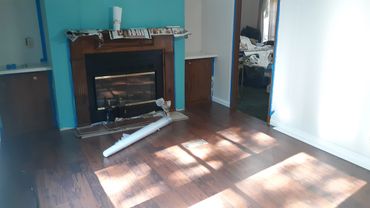 Living room with a fireplace and sunlight on wooden floor during painting.