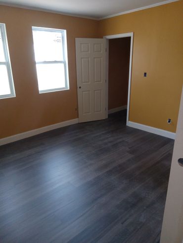 Empty room with mustard walls, white trim, and dark wood flooring.