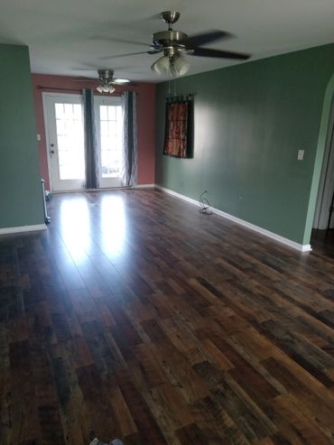 Empty room with wooden floor and green walls, featuring ceiling fans and a glass door.