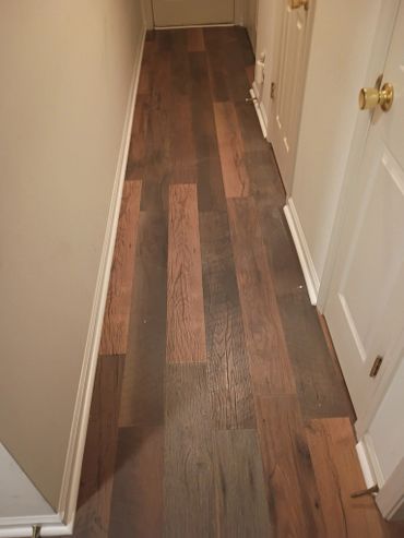 A narrow hallway with dark wooden flooring and white walls.