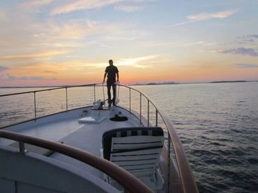 Man standing on fore deck of Juliette, sunset