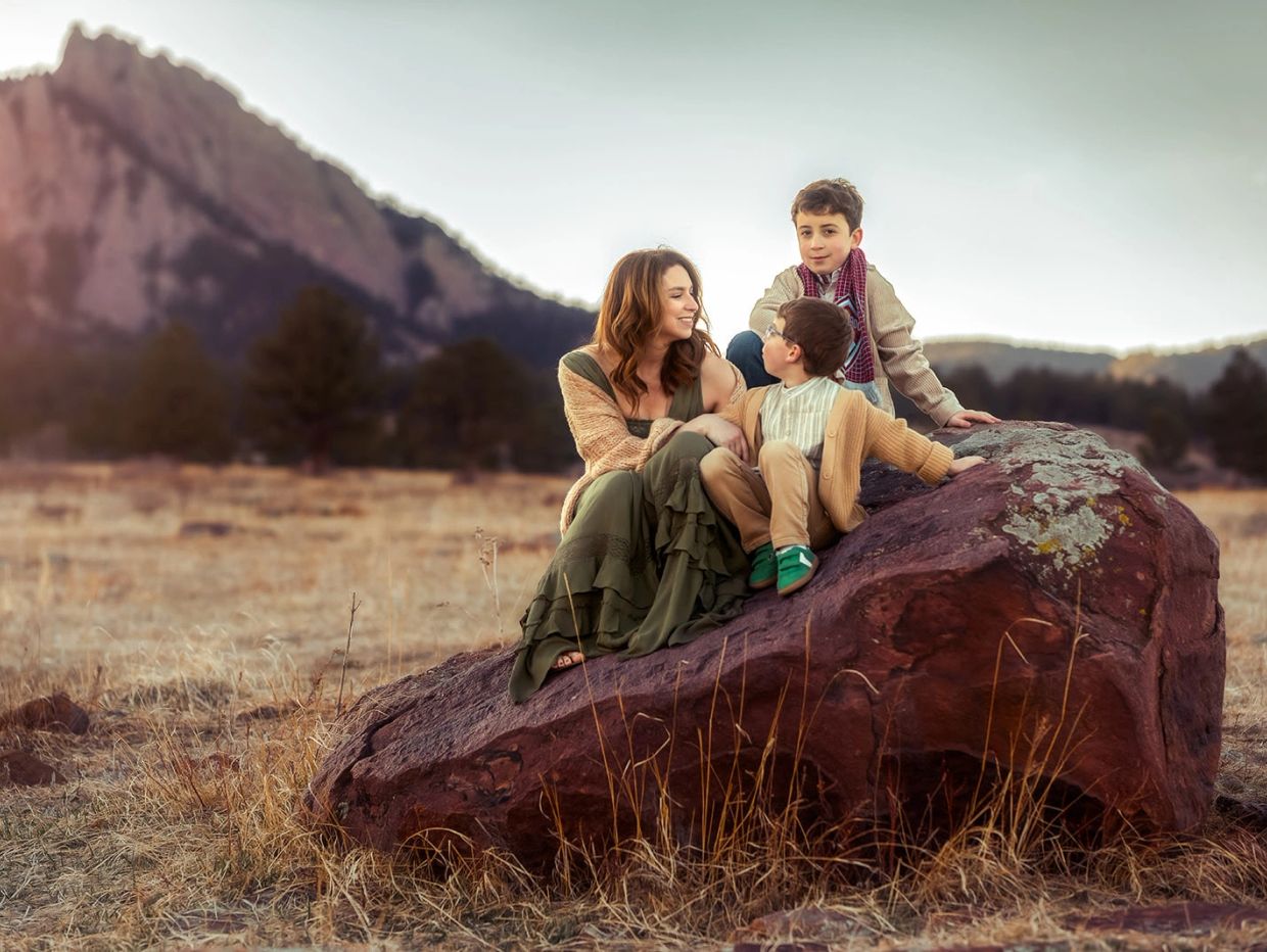 Mother with two boys sitting on a large rock outdoors.