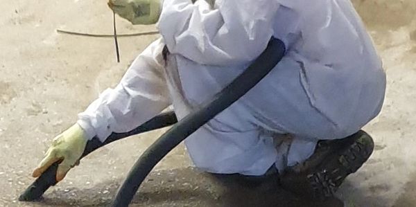 Person in protective suit using a type H vacuum on the ground.