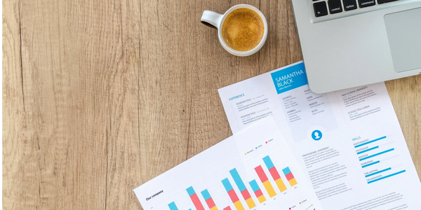 Open laptop with a cup of coffee and some paperwork with graphs