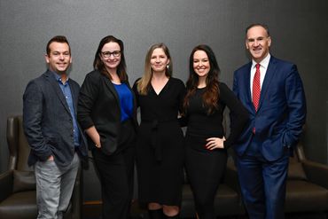 Five professionally dressed individuals posing against a gray wall.