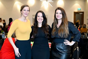 Three women posing and smiling at a social event indoors.