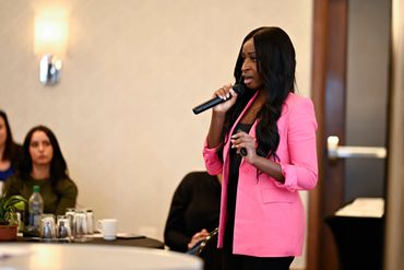 Woman in pink blazer giving a presentation with a microphone.