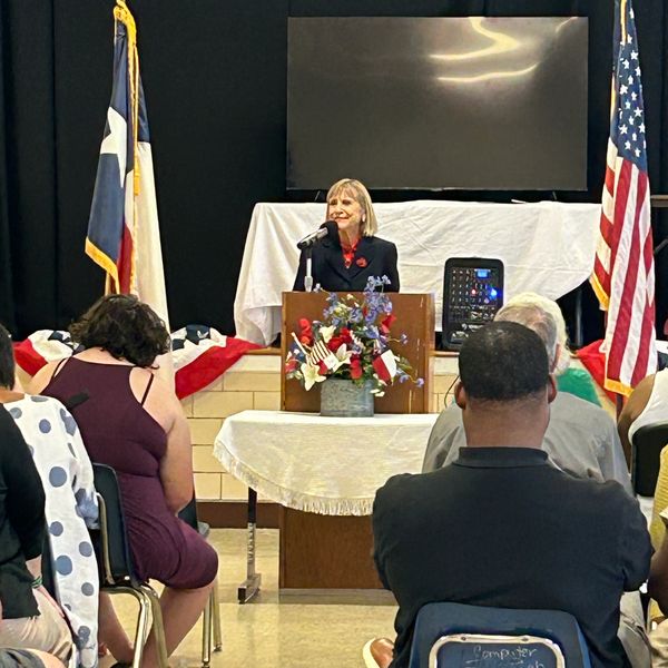 Woman giving speech at a patriotic event with flags and decorations.