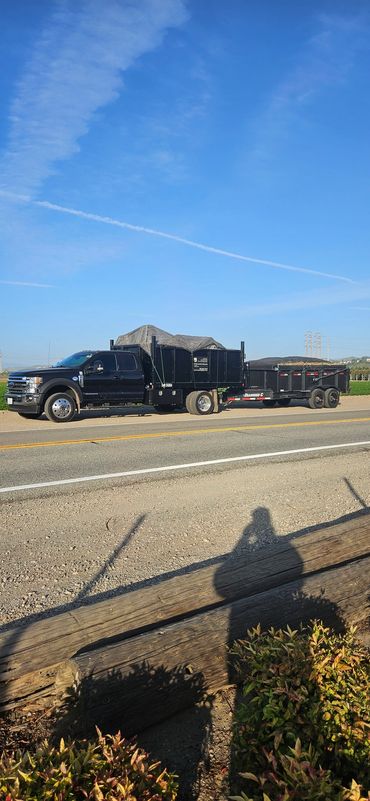 Black truck with a trailer parked on a rural road under a clear blue sky.