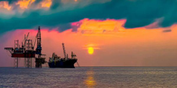 Offshore oil rig and ship at sunset.