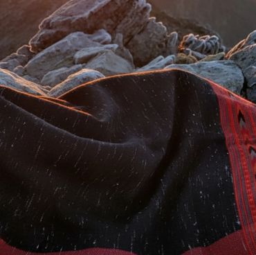 A black and red woven Shawl draped over rocky terrain during sunset.