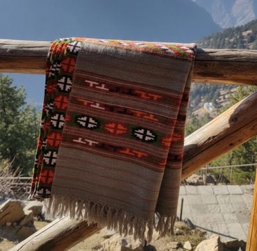 Colorful patterned shawl draped over wooden railing in a mountain setting.
