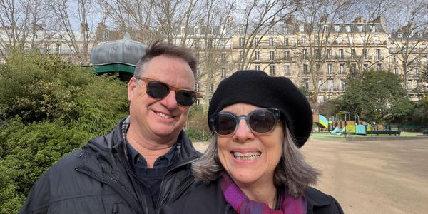 A smiling couple wearing sunglasses outdoors in a park.