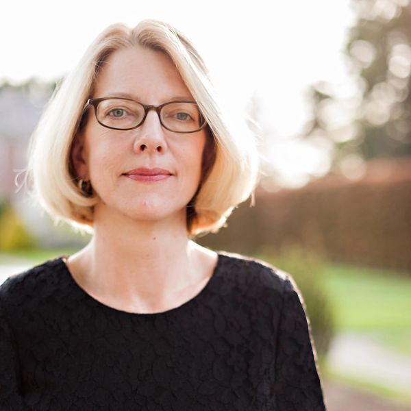 A confident woman with blonde hair and glasses, wearing a black top, standing outdoors.