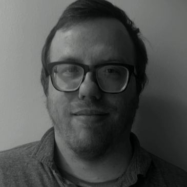 Black and white portrait of a man wearing glasses and a polo shirt.