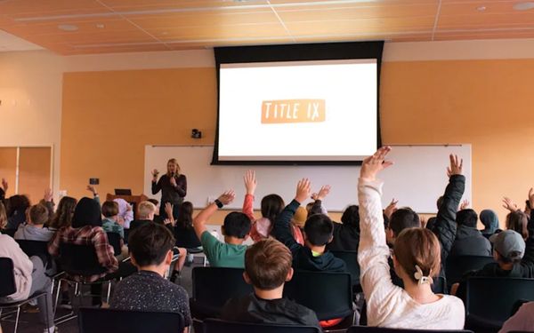 Students raising hands during a Title IX presentation in a classroom.