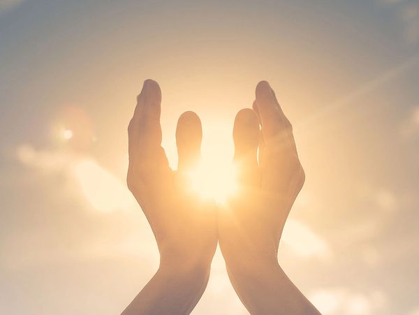 Hands reaching up to the sky with sunlight shining through.