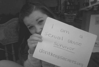 A girl looking at the camera and holding a paper. Text on paper reads I am a sexual abuse survivor