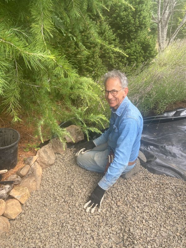 Smiling man gardening with gloves on gravel path.