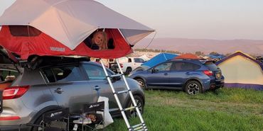lady in a rooftop tent looking out on top of a Kia Sportage camper car.