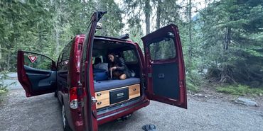 Lady in campervan on the bed with the backdoors open.