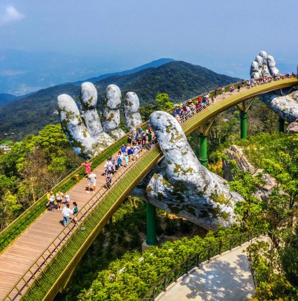 Golden Bridge held by giant hands in a scenic mountainous area.