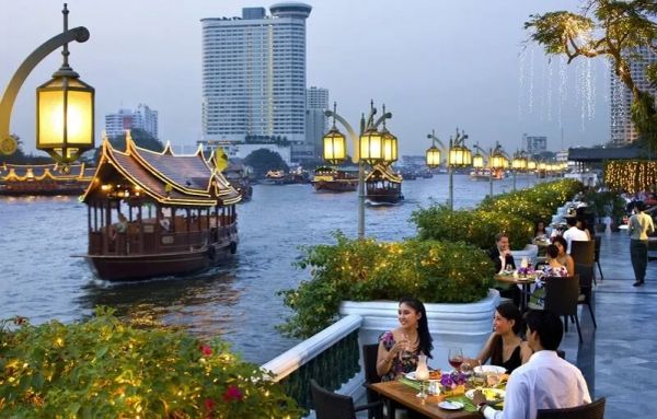 Outdoor riverside dining with illuminated boats at dusk.