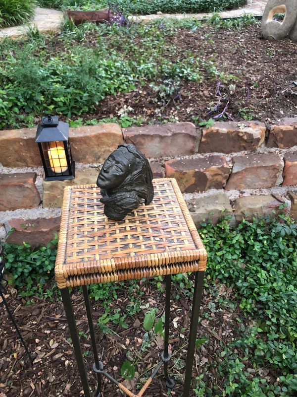 Sculpted head on wicker table outdoors near brick wall and lantern.