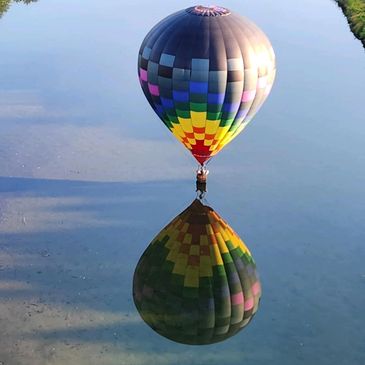 Colorful hot air balloon reflected perfectly on calm water.