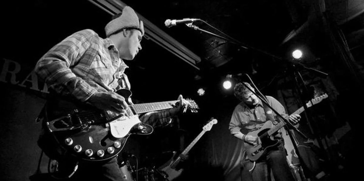 Two musicians passionately playing electric guitars on stage in a dimly lit venue.