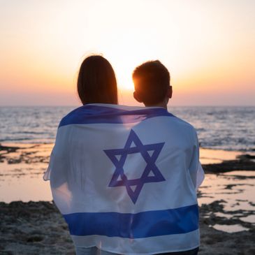 Children draped in the flag of the State of Israel looking at the sunset over the Mediterranean Sea