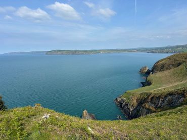 Coastal cliffs overlooking a blue ocean under a clear sky.